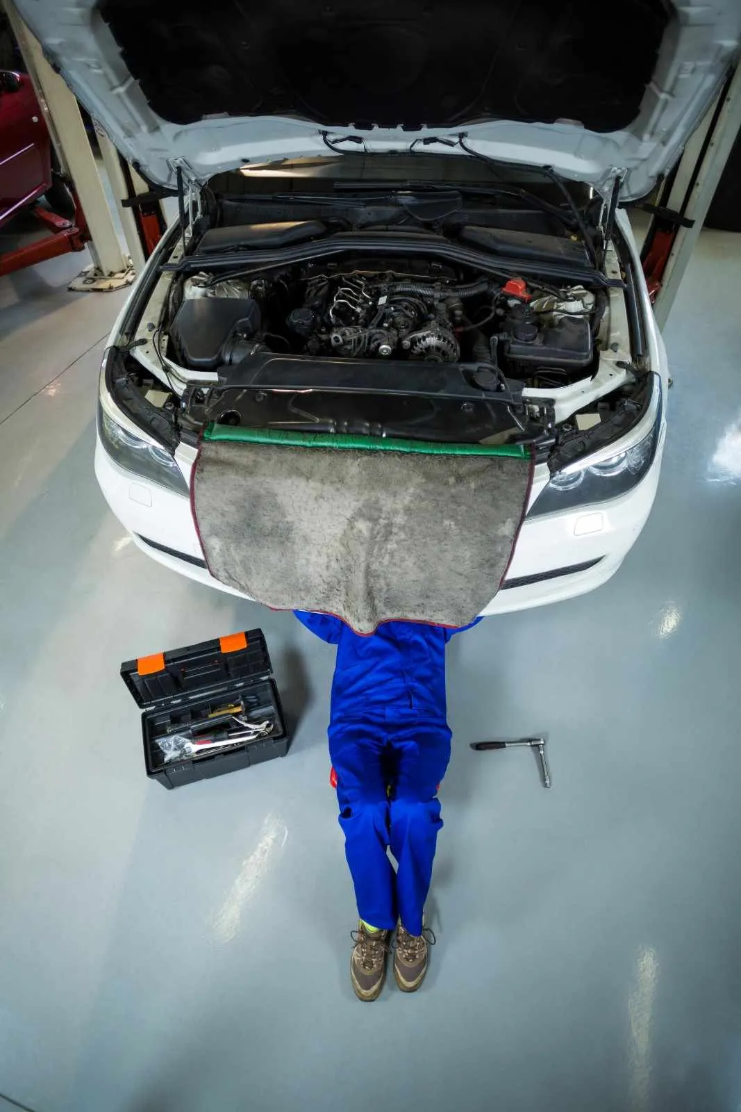 Mechanic lying under the front of a white car with its bonnet open